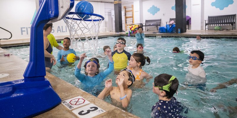 Kids playing in the pool around a floating basketball hoop