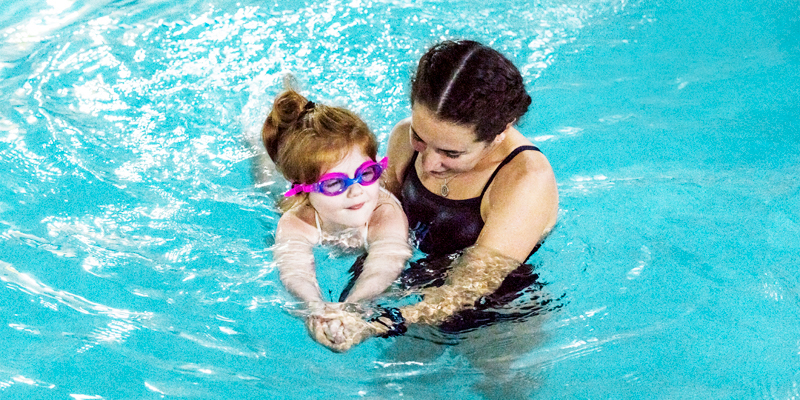 An instructor helps a young girl in goggles float