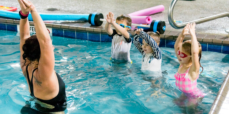 Kids and their instructor raise their arms in a swim class