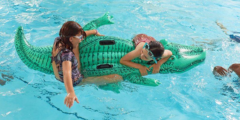 Two campers ride an inflatable alligator in the pool