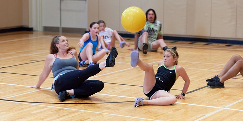Campers sitting on the gym floor passing a ball with their feet
