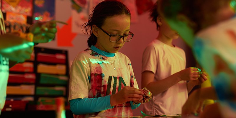 A camper in glasses works on a craft project