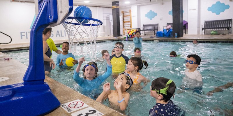 Campers playing in the pool around a floating basketball hoop