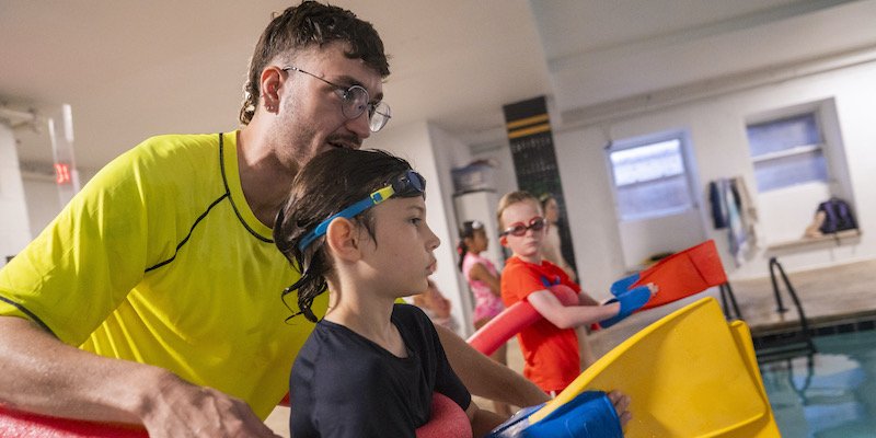 A counselor helps a camper during a pool activity