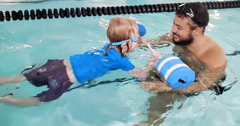 A coach helps a young boy practice kicking with a float