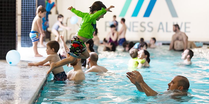 A boy leaps into the pool toward his dad at family swim